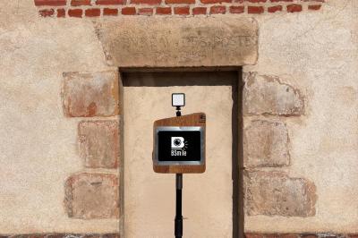 Borne photo en bois avec écran et flash, installée devant une porte en pierre et un mur en briques.