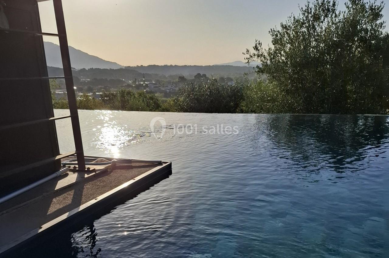 Piscine à débordement reflétant le soleil, avec vue sur un paysage vallonné et des arbres en arrière-plan.