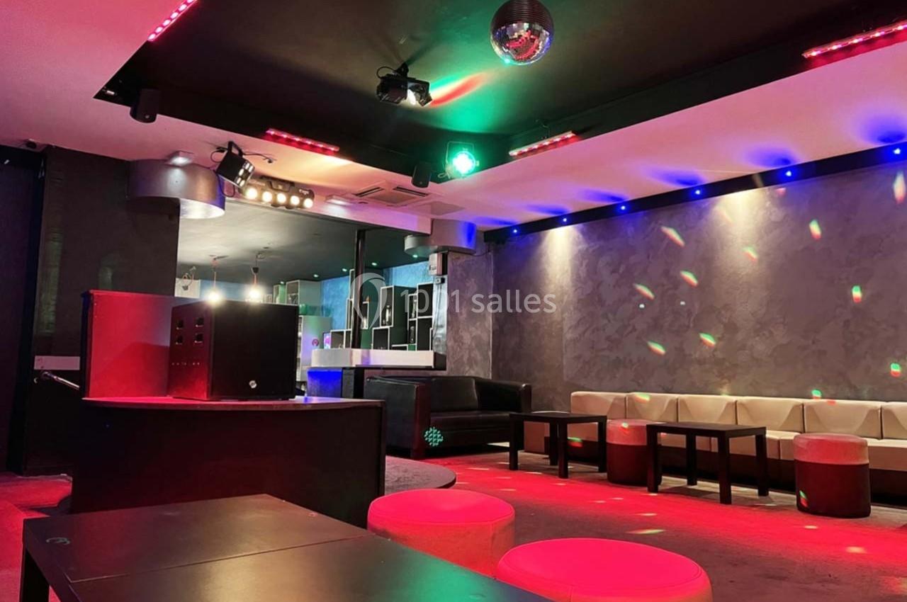 Salle de réception moderne avec éclairage coloré, banquettes en cuir clair et piste de danse équipée d'une boule disco.