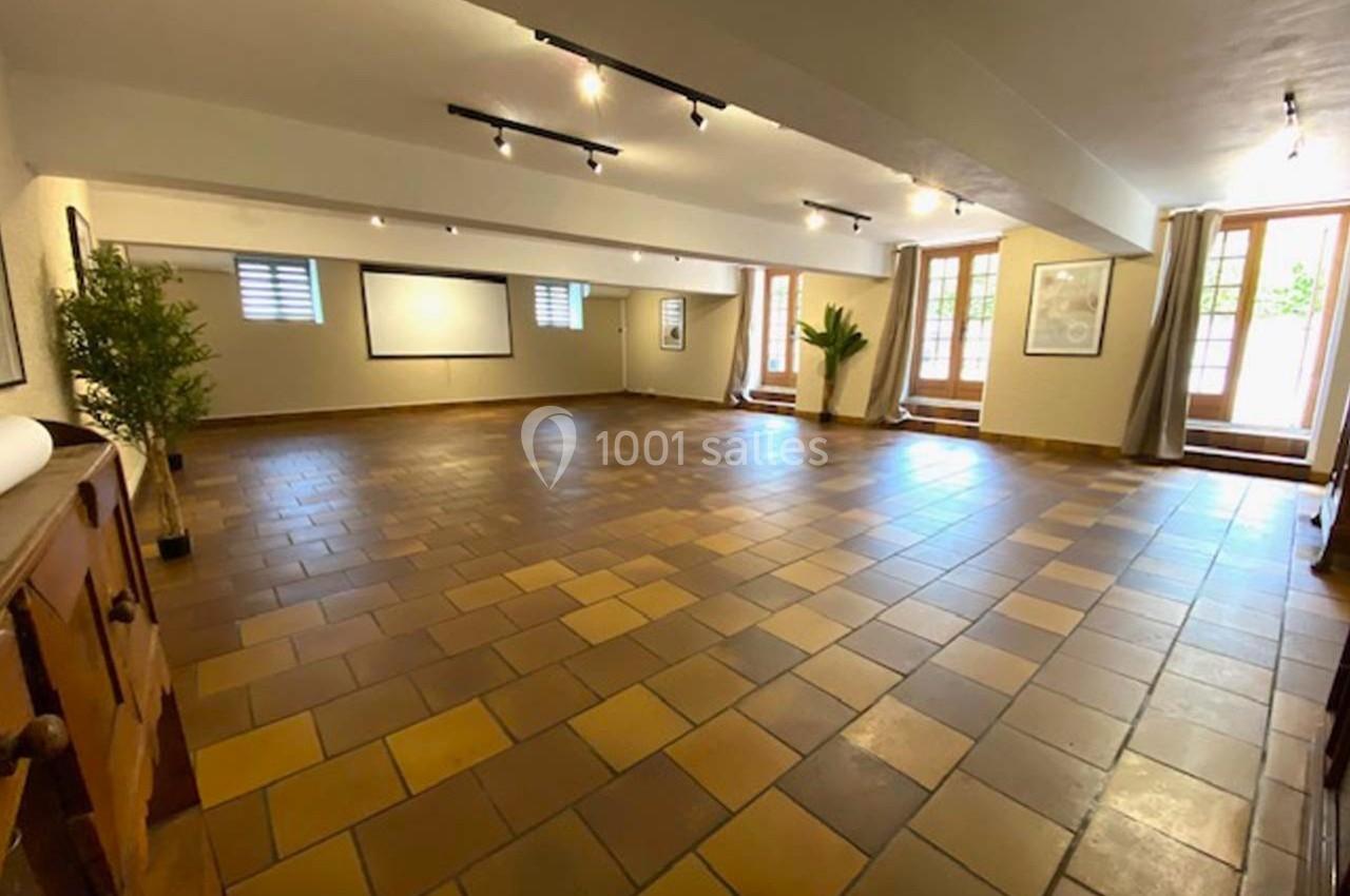 Salle spacieuse avec sol en carrelage marron, murs clairs, grandes fenêtres et éclairage au plafond.