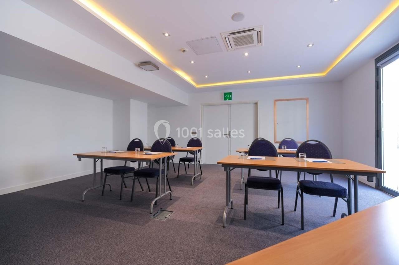 Salle de réunion lumineuse avec tables en bois, chaises bleues et verres disposés pour une présentation ou formation.