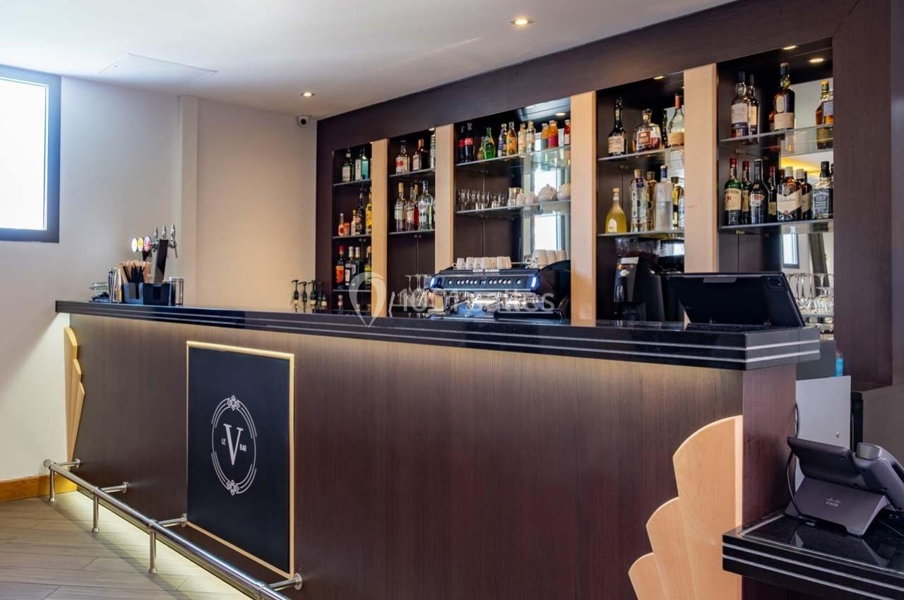 Comptoir de bar moderne avec étagères remplies de bouteilles d'alcool et machine à café en arrière-plan.