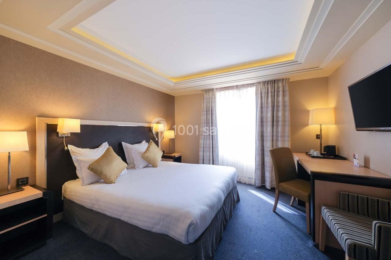 Chambre d'hôtel lumineuse avec un grand lit, des lampes de chevet, un bureau, une télévision et une fenêtre avec rideaux.
