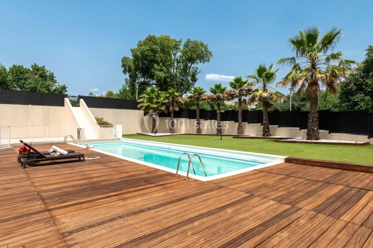 Piscine extérieure entourée d'une terrasse en bois, de chaises longues et de palmiers sous un ciel dégagé.