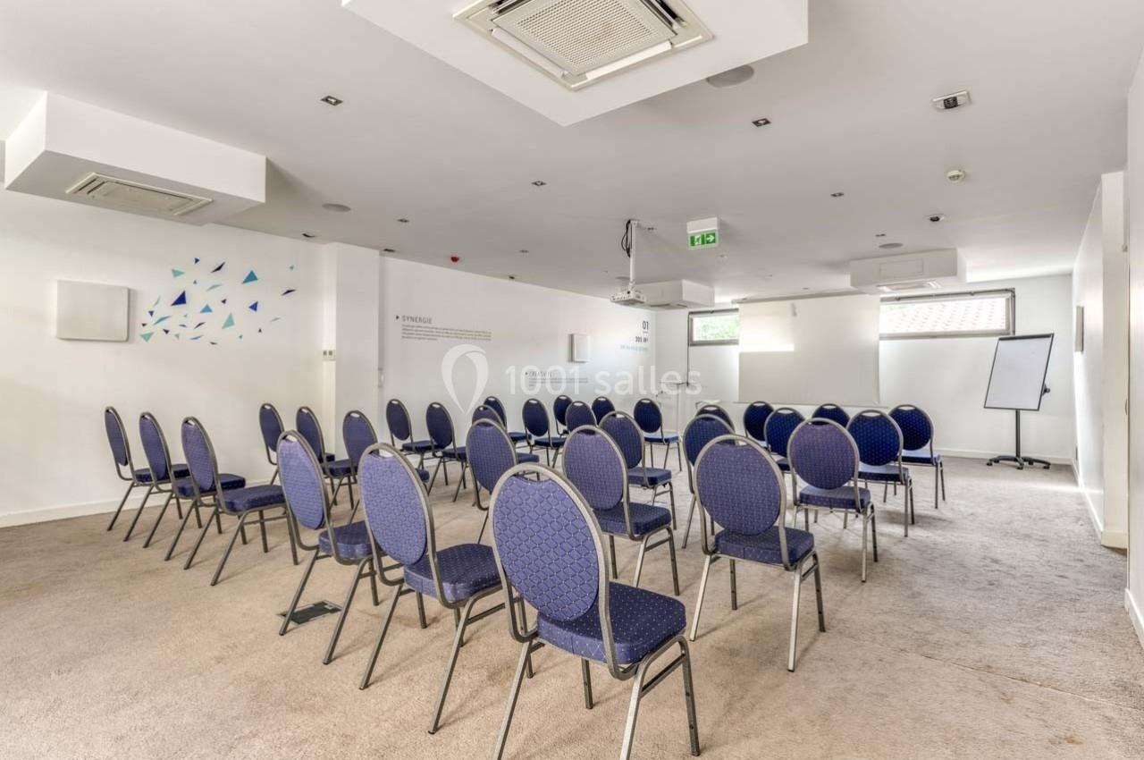 Salle de réunion lumineuse avec des chaises disposées en rangées face à un tableau blanc et un projecteur.