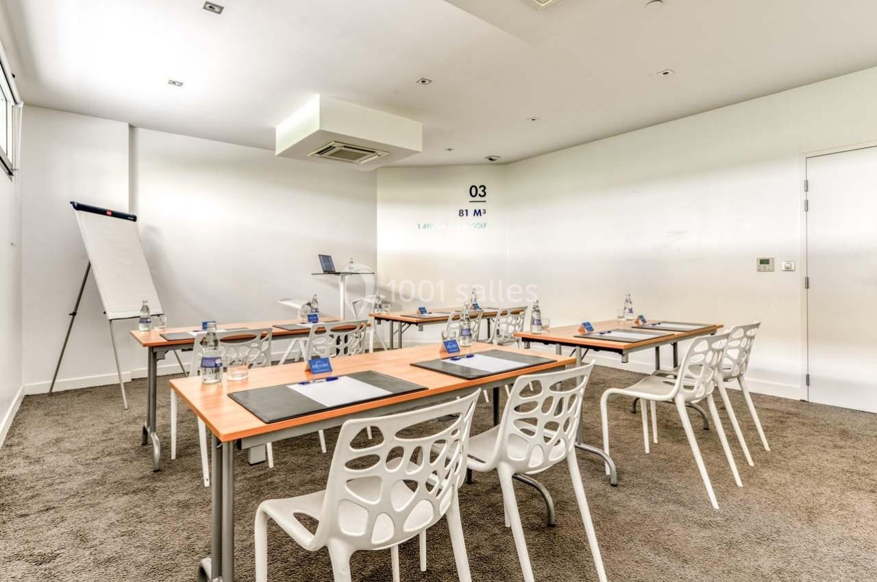 Salle de réunion lumineuse avec tables, chaises modernes, paperboard, bouteilles d'eau et matériel de prise de notes.