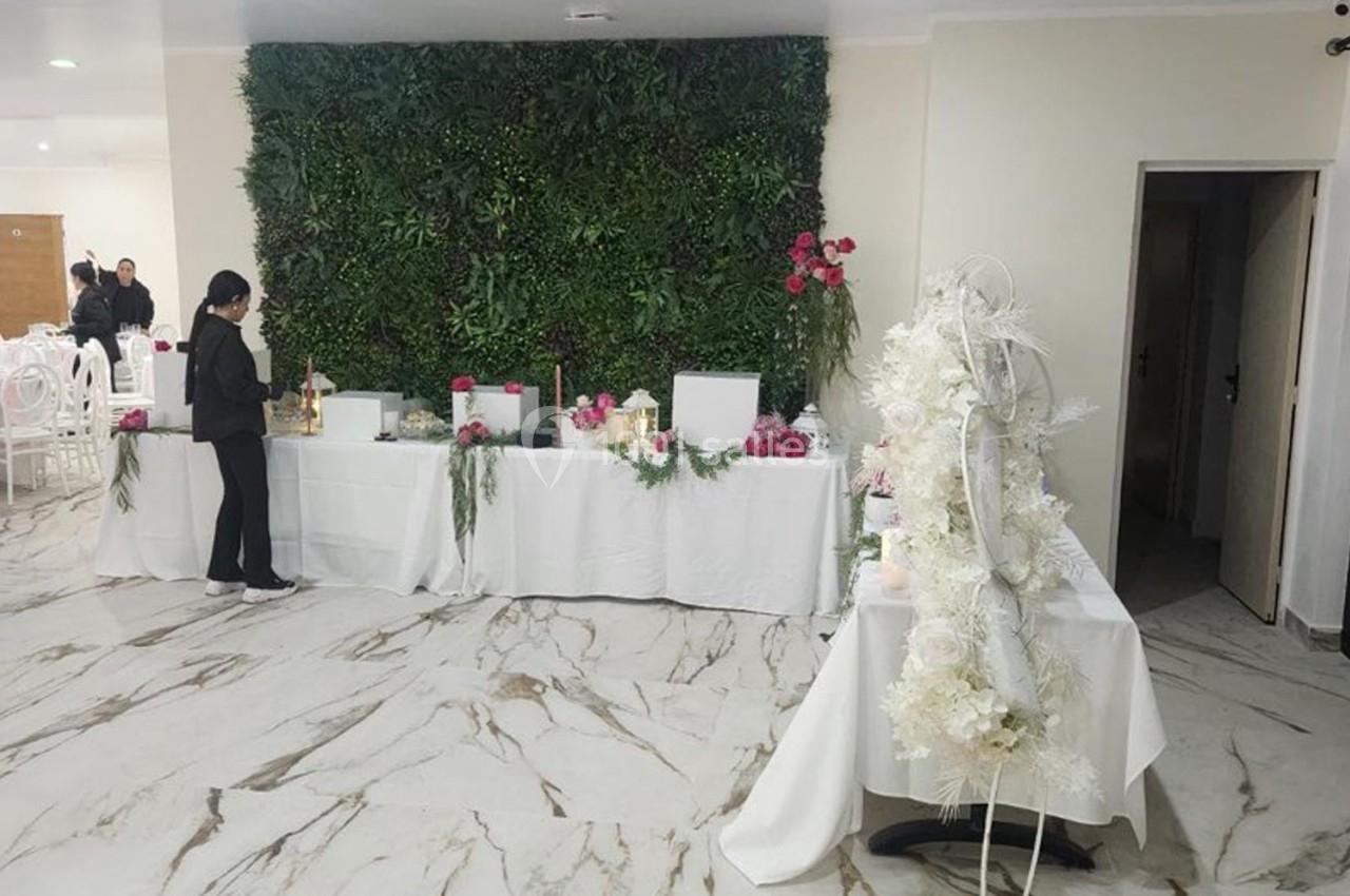 Salle décorée avec un mur végétal, tables blanches ornées de fleurs et une personne debout à côté.