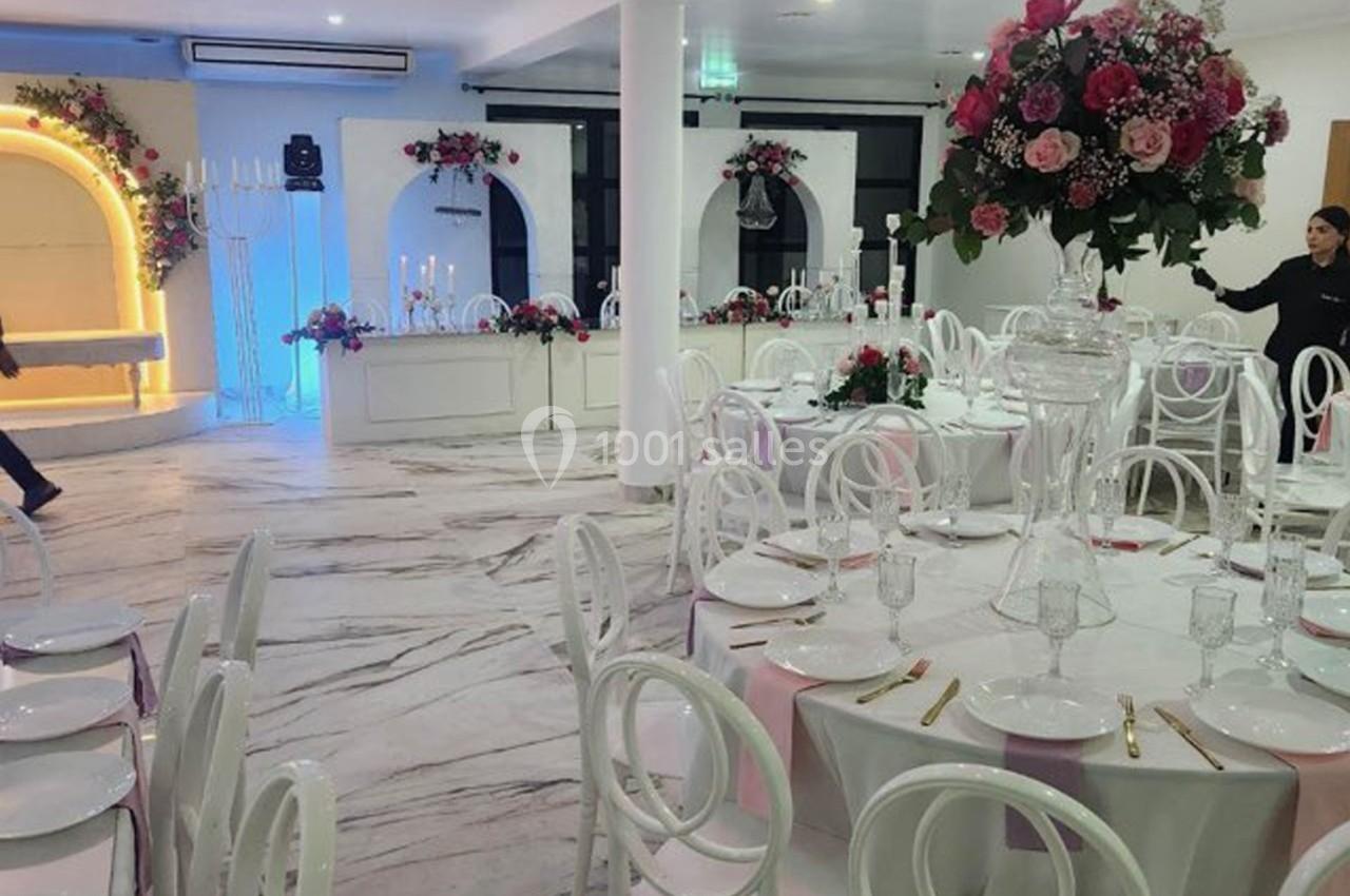 Salle de réception décorée avec des tables rondes, des chaises blanches, des fleurs et des bougies.