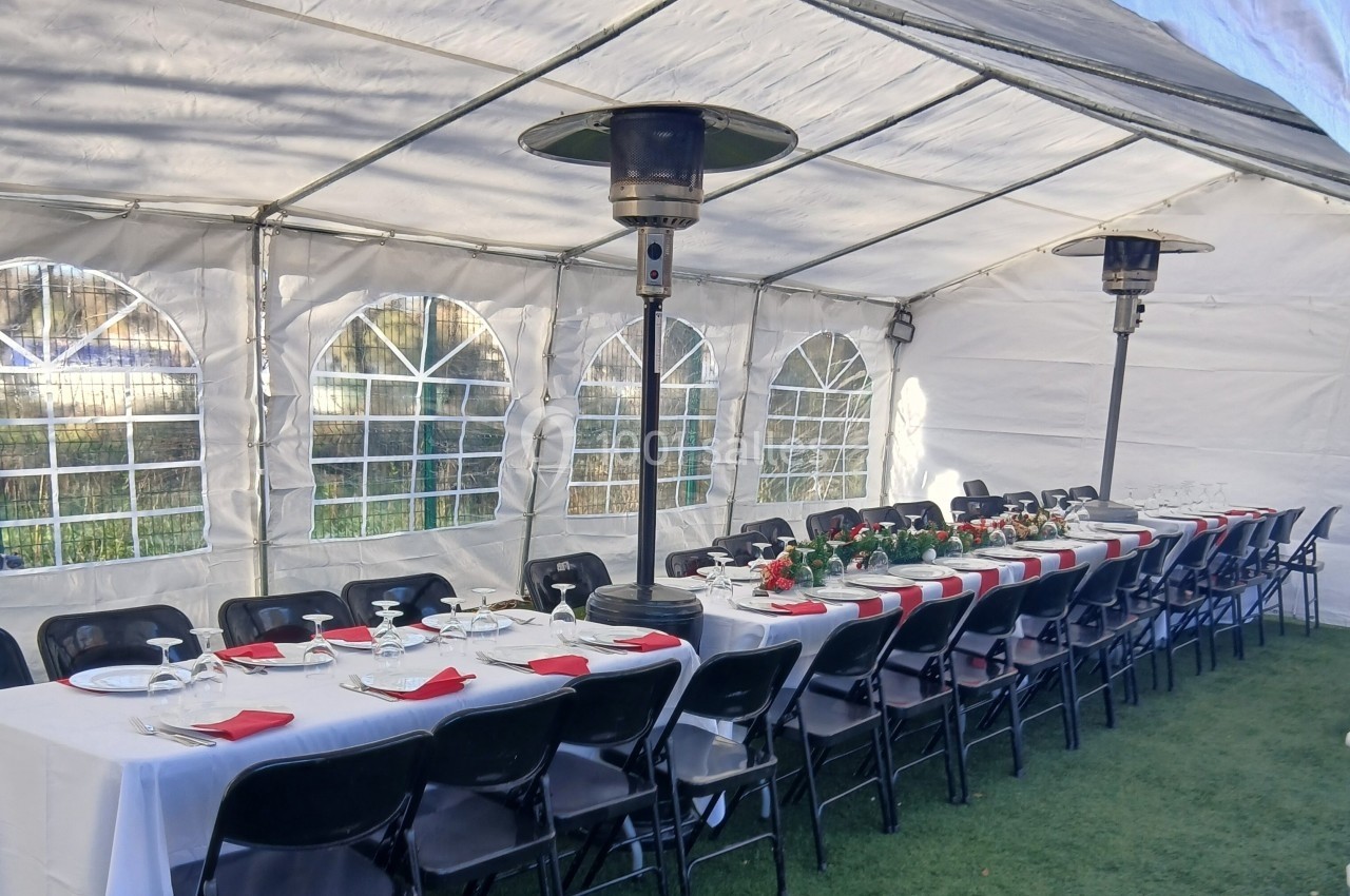 Tables dressées avec nappes blanches, serviettes rouges et chauffages extérieurs sous une tente blanche.