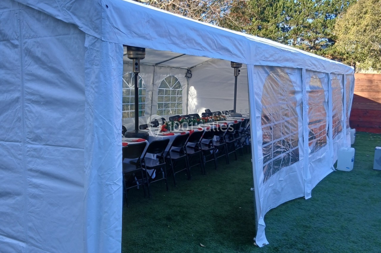 Tente blanche aménagée avec des tables et chaises alignées pour un événement en extérieur.