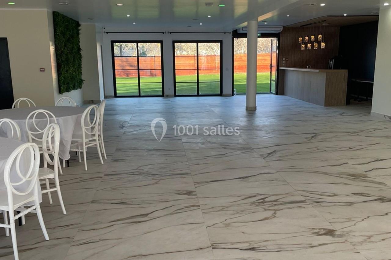 Salle lumineuse avec sol en marbre, chaises blanches, mur végétal et baies vitrées donnant sur un espace extérieur.
