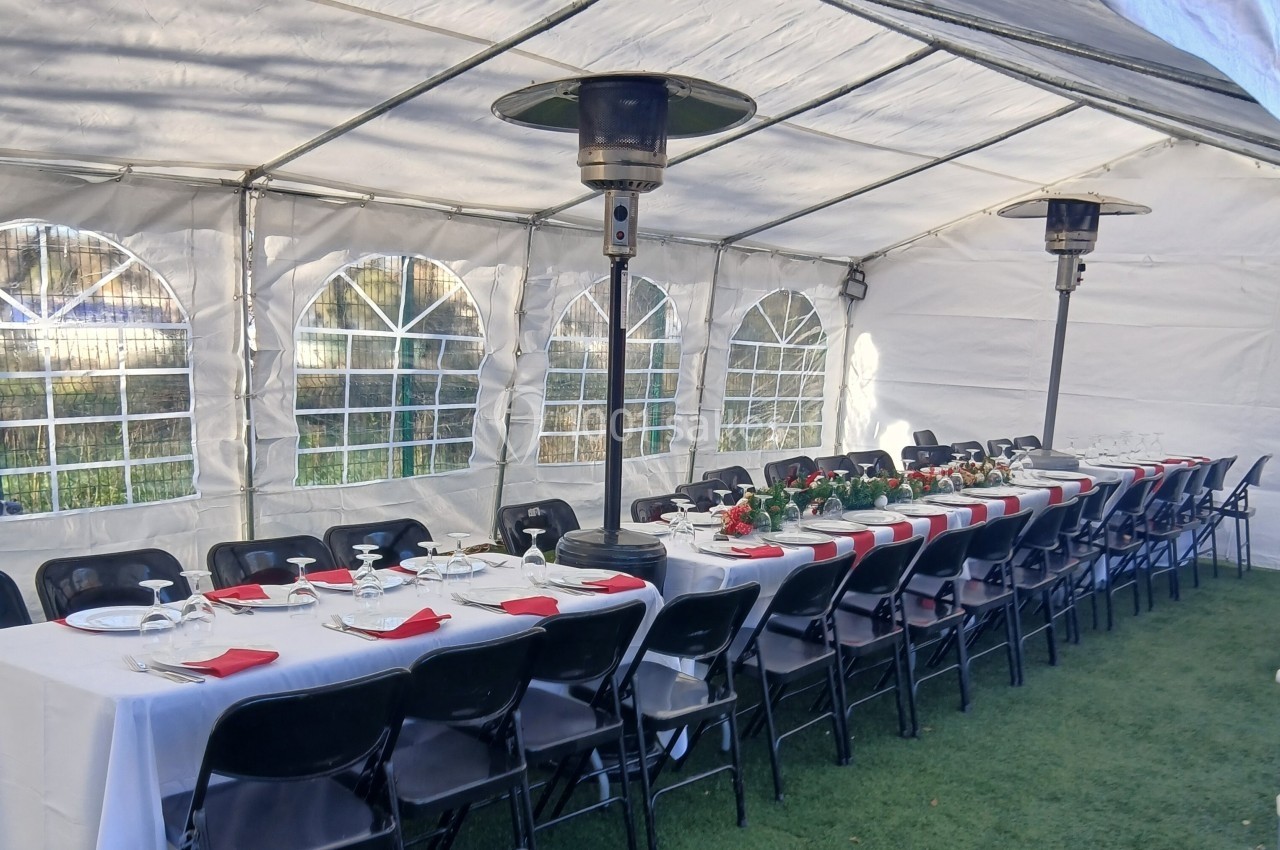 Tables longues dressées avec nappes blanches, serviettes rouges et chaises noires sous une tente équipée de chauffages.