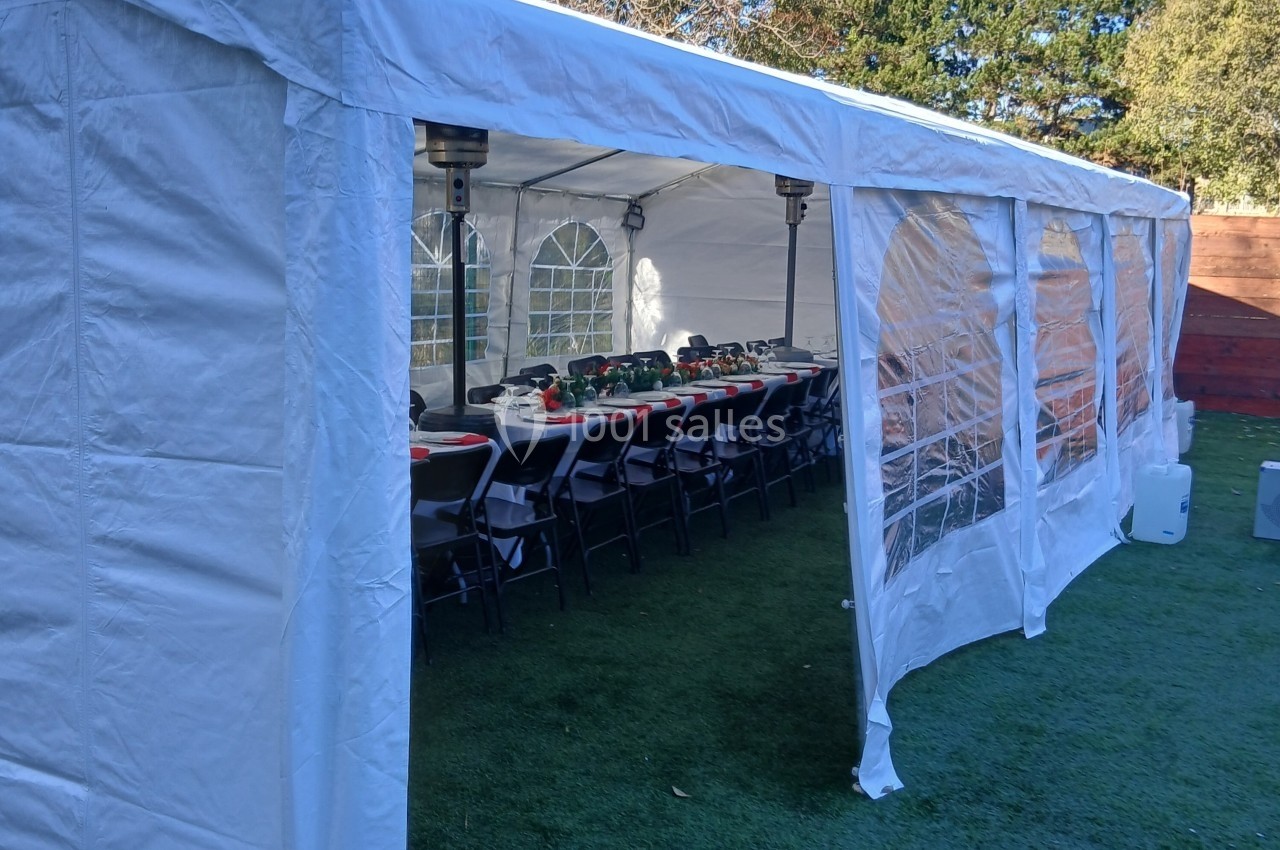 Tente blanche installée sur une pelouse, abritant des tables et chaises alignées pour un événement.