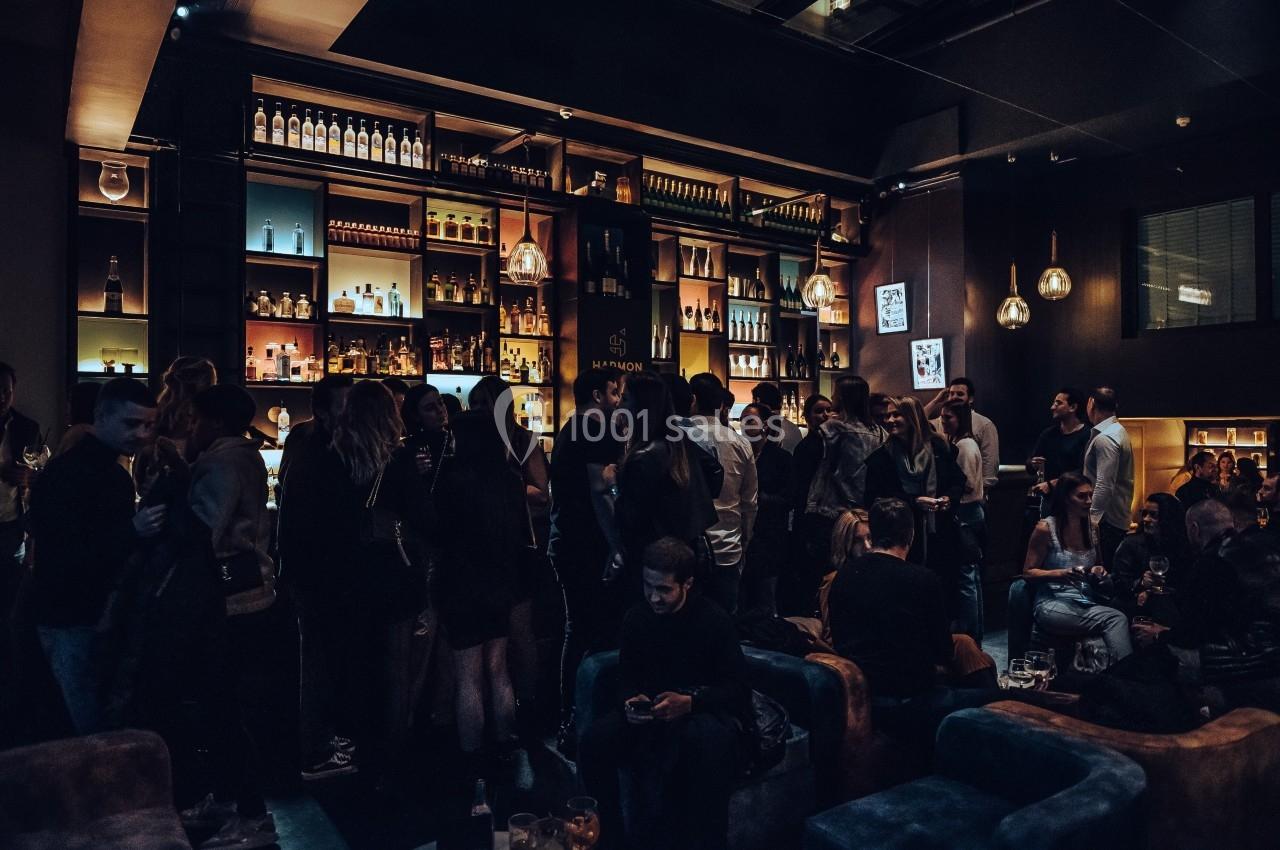 Groupe de personnes rassemblées dans un bar à l'ambiance tamisée, entourées de bouteilles et de lumières suspendues.
