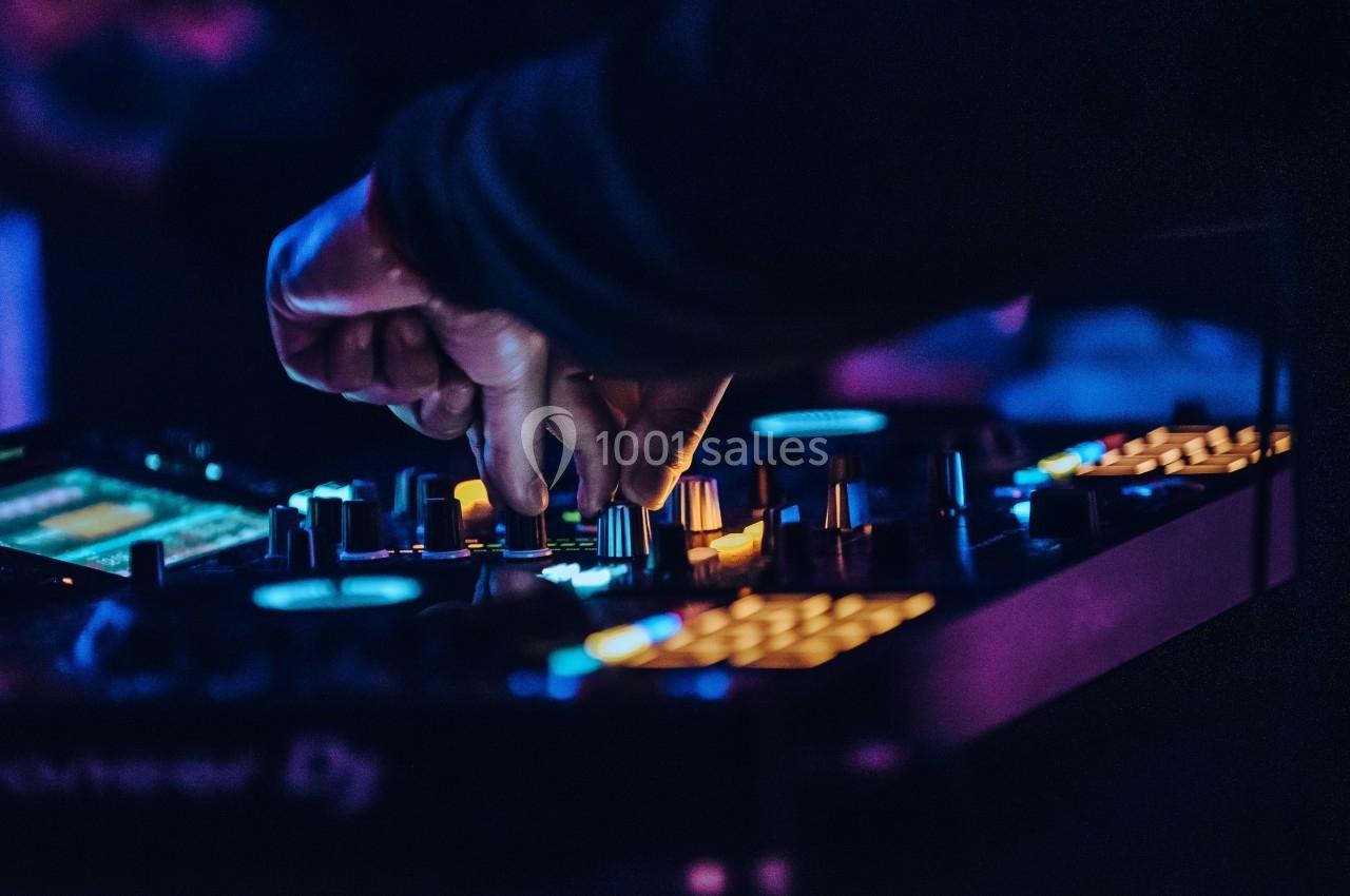Main ajustant des commandes sur une table de mixage éclairée dans une ambiance sombre et lumineuse.