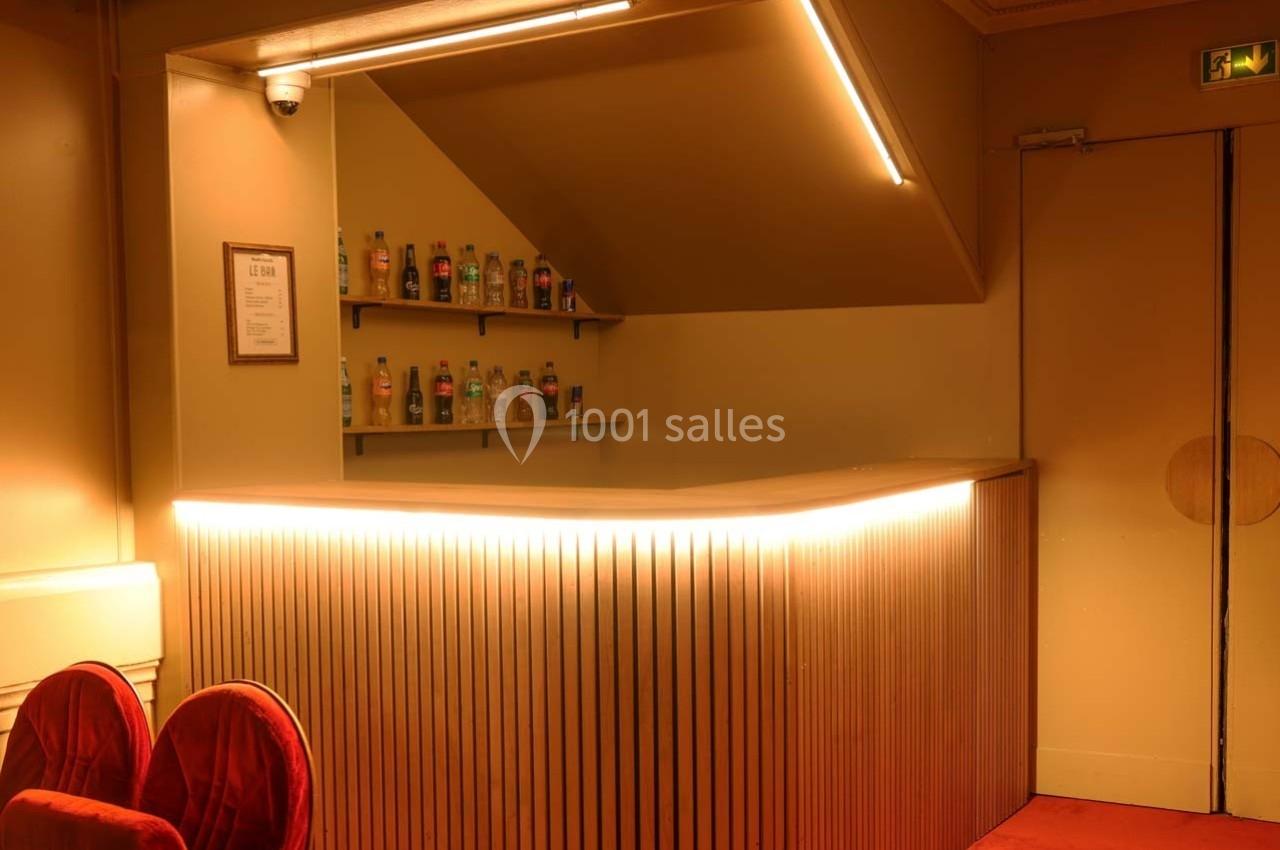 Bar de la Grande salle du Palais des Glaces Comptoir de bar en bois éclairé, avec étagères contenant des bouteilles, dans un intérieur au ton chaleureux.