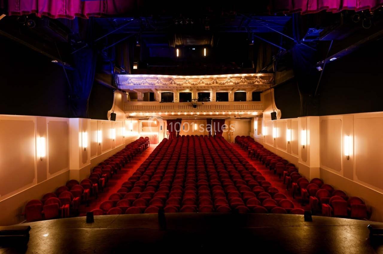 Grande salle du Palais des Glaces Salle de théâtre vide avec rangées de sièges rouges, vue depuis la scène, éclairage tamisé et balcon illuminé.