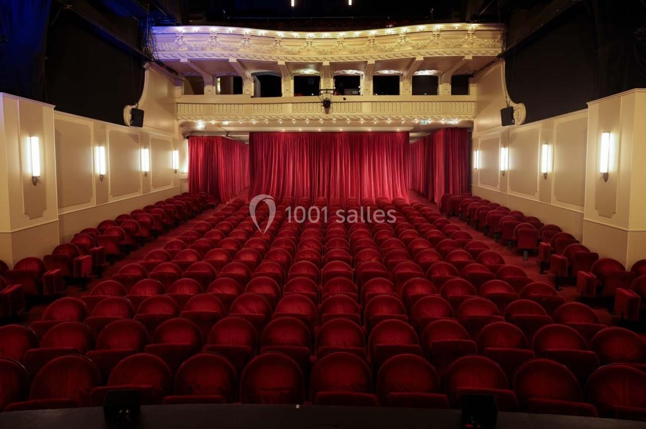 Grande salle du Palais des Glaces en jauge 270 Salle de théâtre vide avec des rangées de fauteuils rouges et une scène fermée par un rideau rouge.