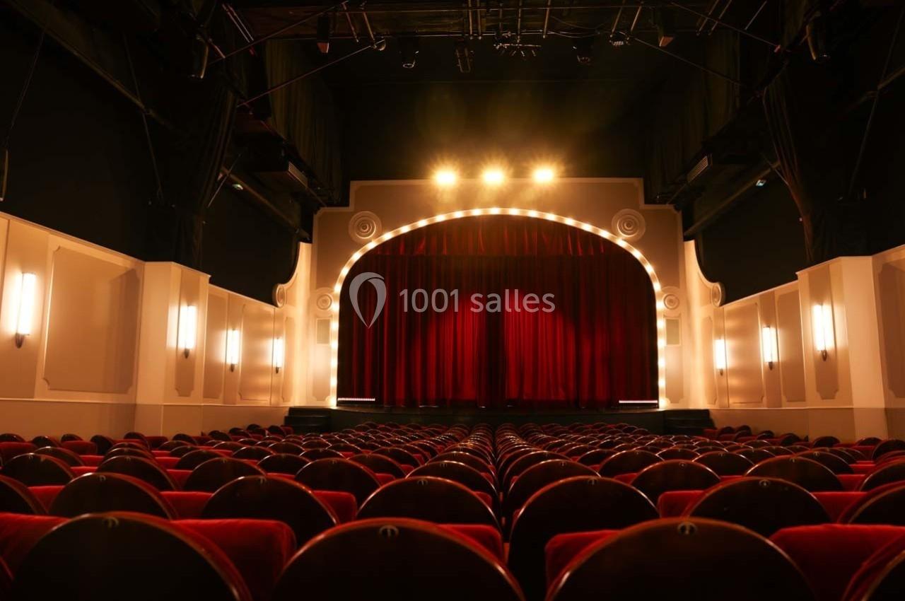 Grande Salle du Palais des Glaces Salle de théâtre vide avec rangées de sièges rouges et une scène éclairée par des projecteurs.