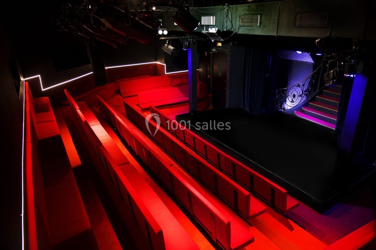 Petit Palais des Glaces Salle de spectacle vide avec des sièges rouges, une scène éclairée et un escalier sur le côté.