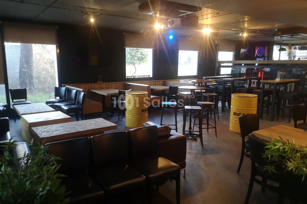Salle de bar aménagée avec des tables, chaises, tonneaux décoratifs et éclairage tamisé.