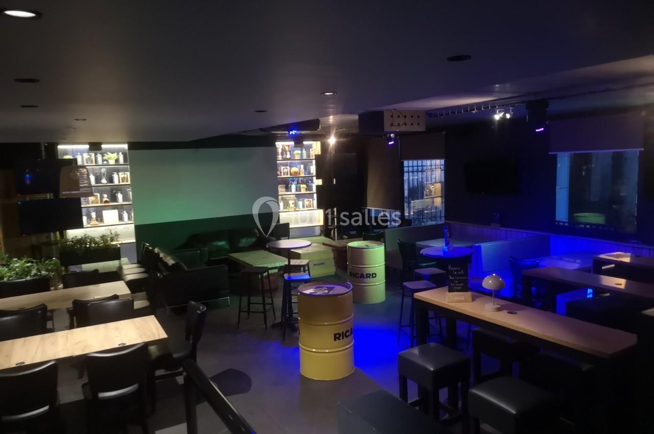 Salle de bar moderne avec tables en bois, tonneaux jaunes en guise de tables, éclairage tamisé et étagères illuminées.