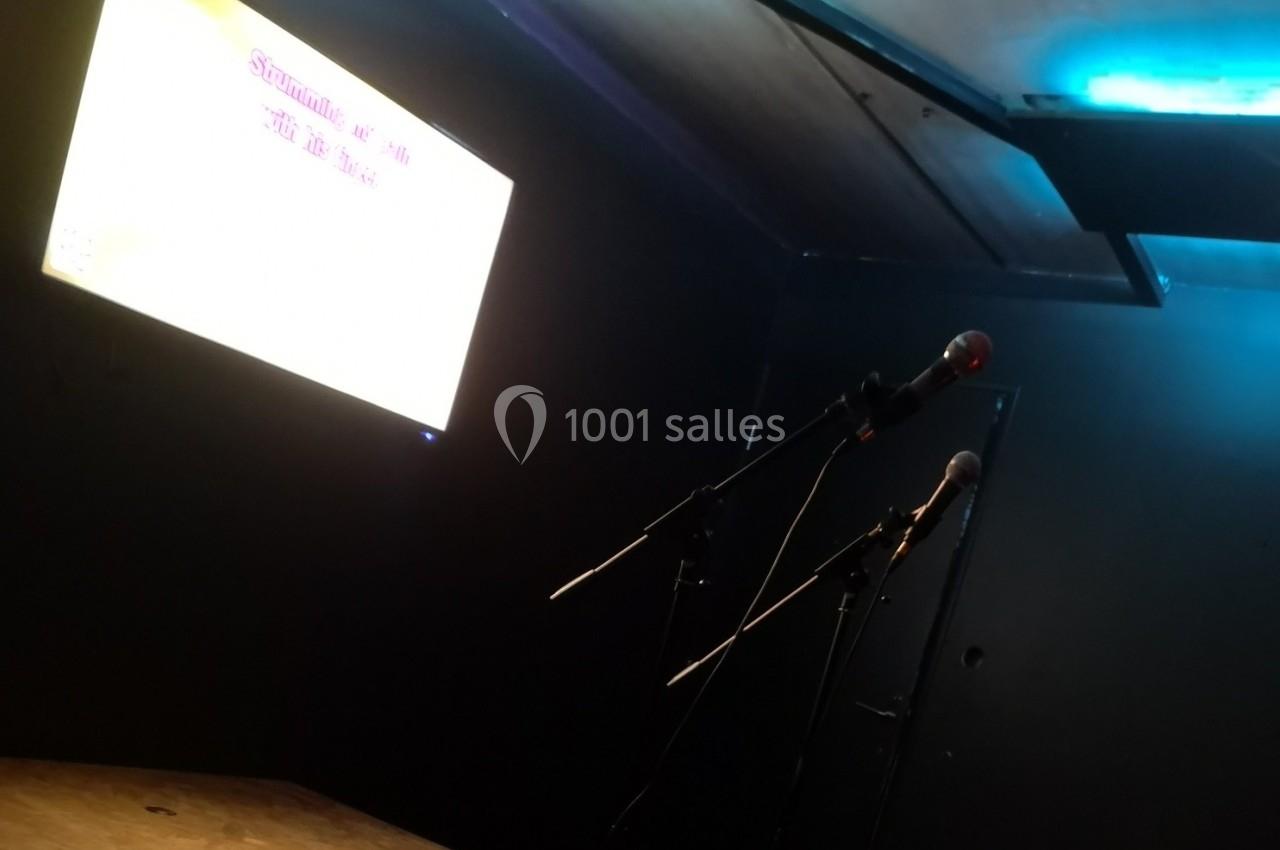 Deux micros sur scène dans une salle sombre, avec un écran lumineux affichant du texte en arrière-plan.