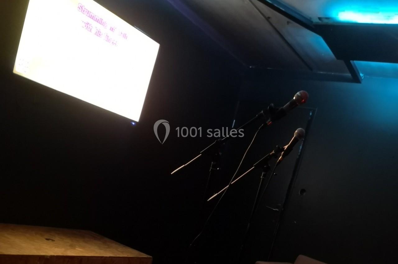 Deux micros sur pied dans une salle sombre, éclairée par un écran lumineux affichant un texte flou.