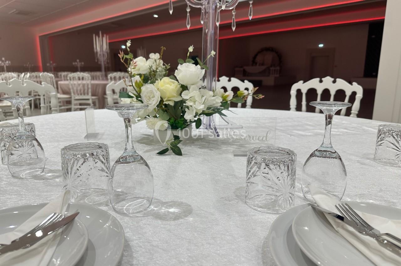 Table dressée avec nappes blanches, vaisselle élégante, verres en cristal et centre de table floral dans une salle de…