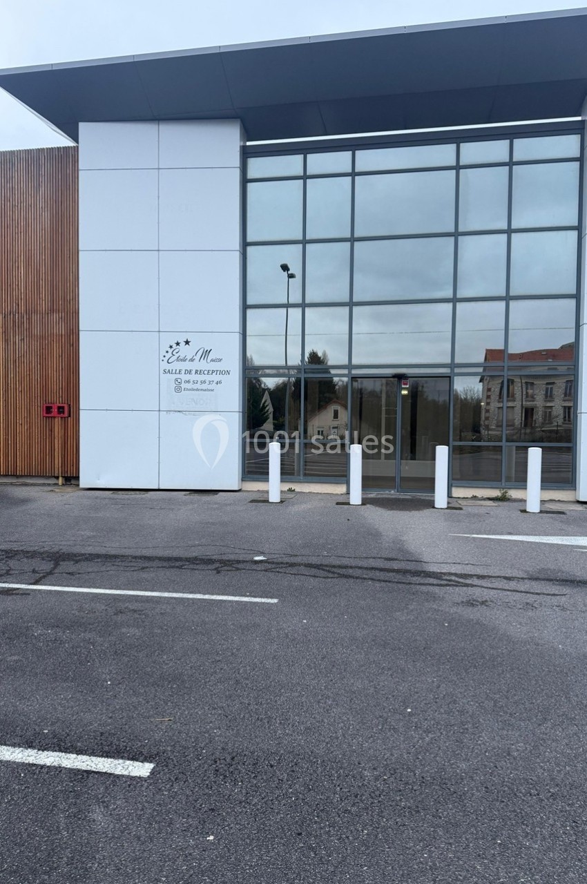 Façade vitrée d'une salle de réception moderne avec des panneaux en bois et un parking à l'avant.