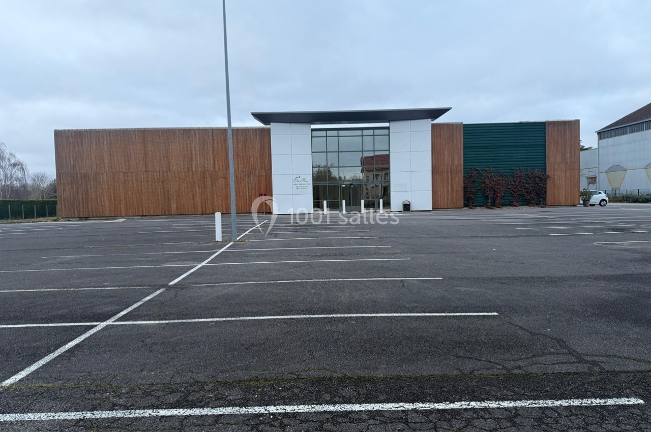 Façade d'un bâtiment moderne avec des murs en bois et en verre, entouré d'un grand parking vide.