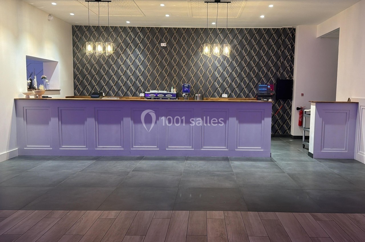 Comptoir violet dans une pièce moderne avec carrelage sombre et mur à motifs géométriques éclairé par des suspensions.
