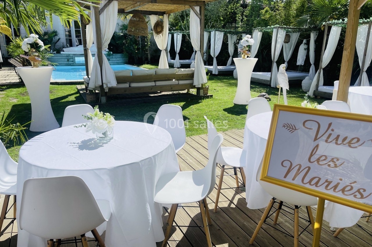 Tables décorées en extérieur avec nappes blanches, panneau ’Vive les Mariés’ et piscine en arrière-plan.