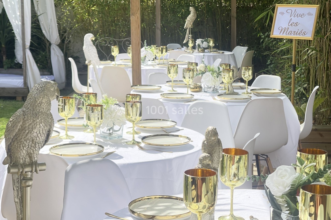 Tables de réception décorées avec des assiettes dorées, des verres assortis et des statues d'oiseaux, en extérieur.