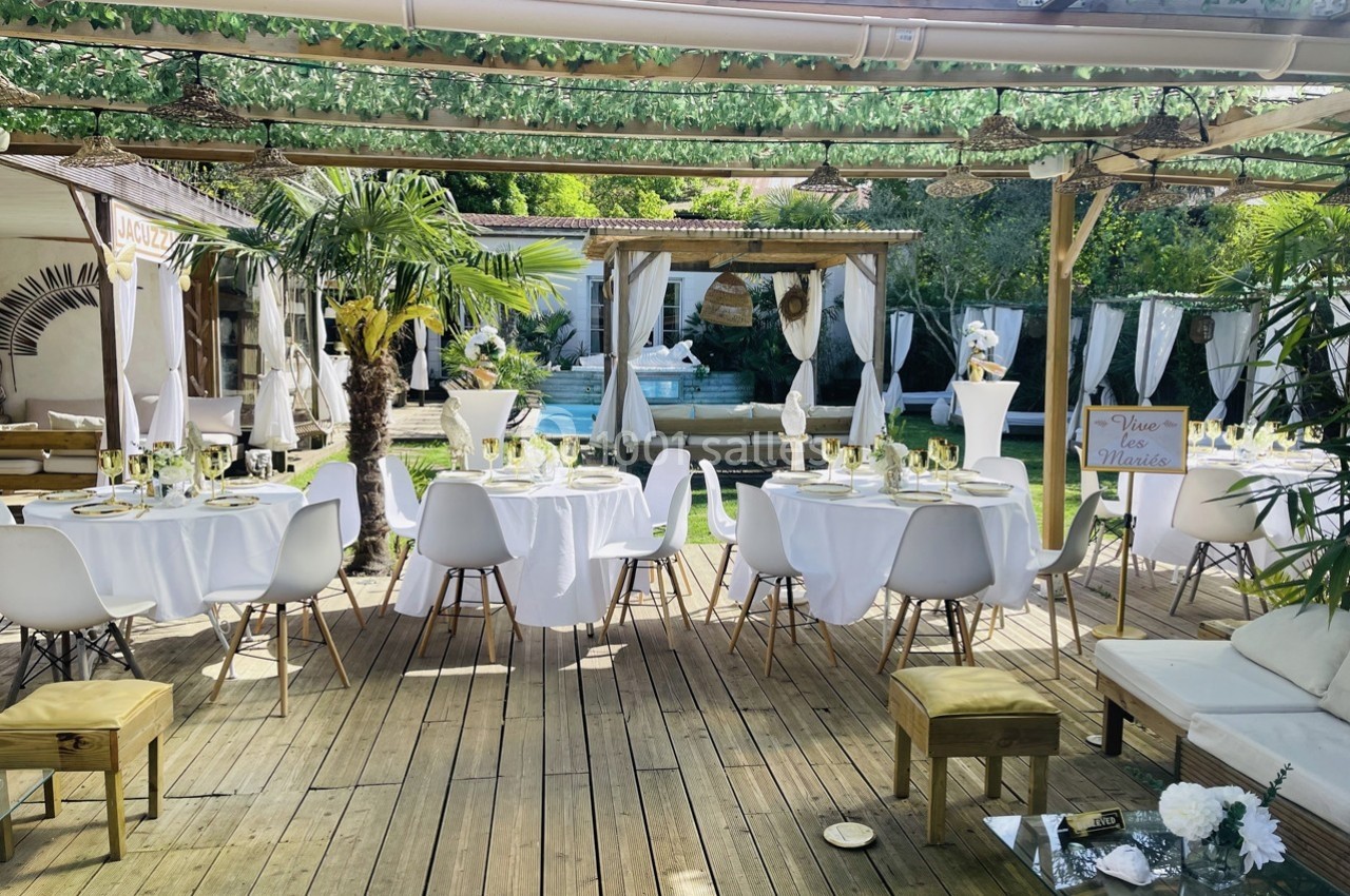 Terrasse aménagée avec tables dressées pour un événement, entourée de végétation et décorations élégantes.