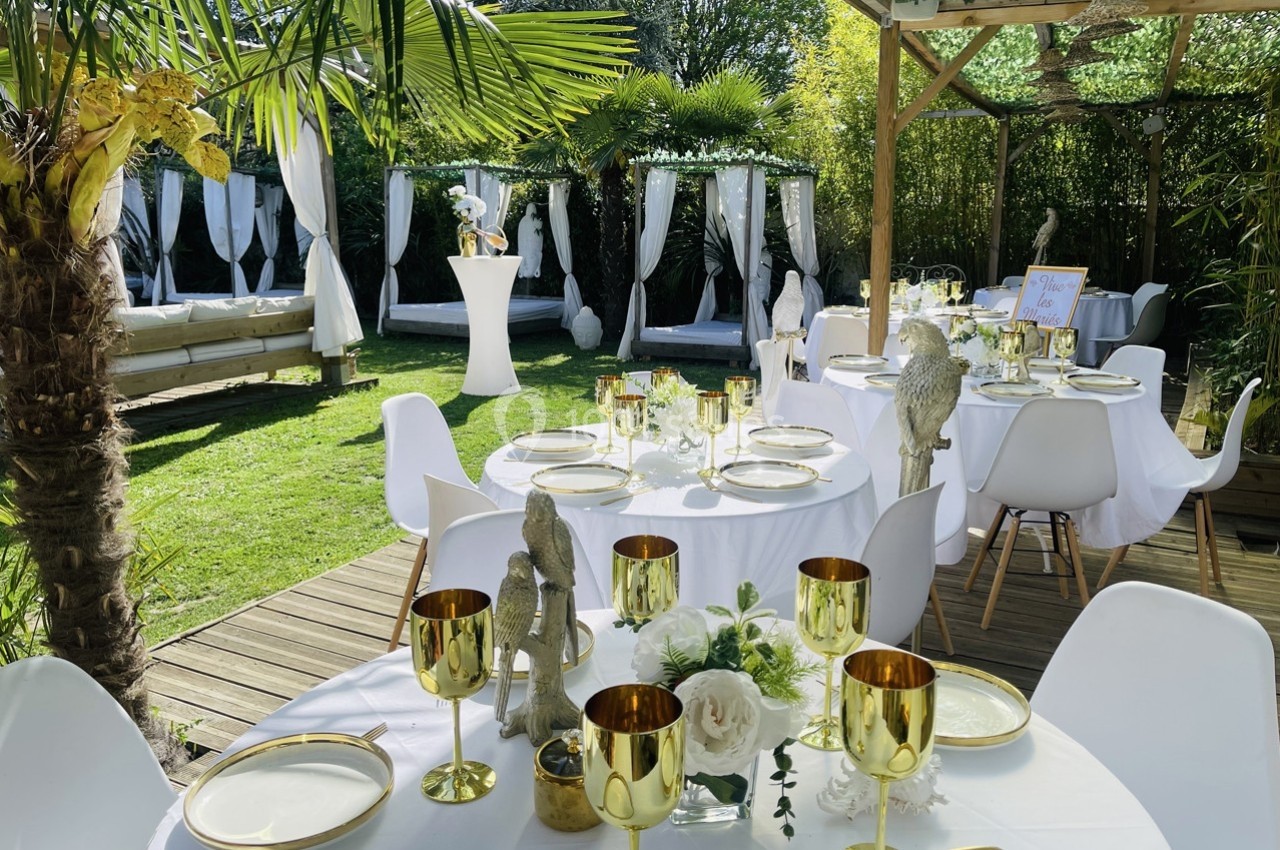 Tables décorées avec élégance dans un jardin, ornées de vaisselle dorée et entourées de végétation luxuriante.