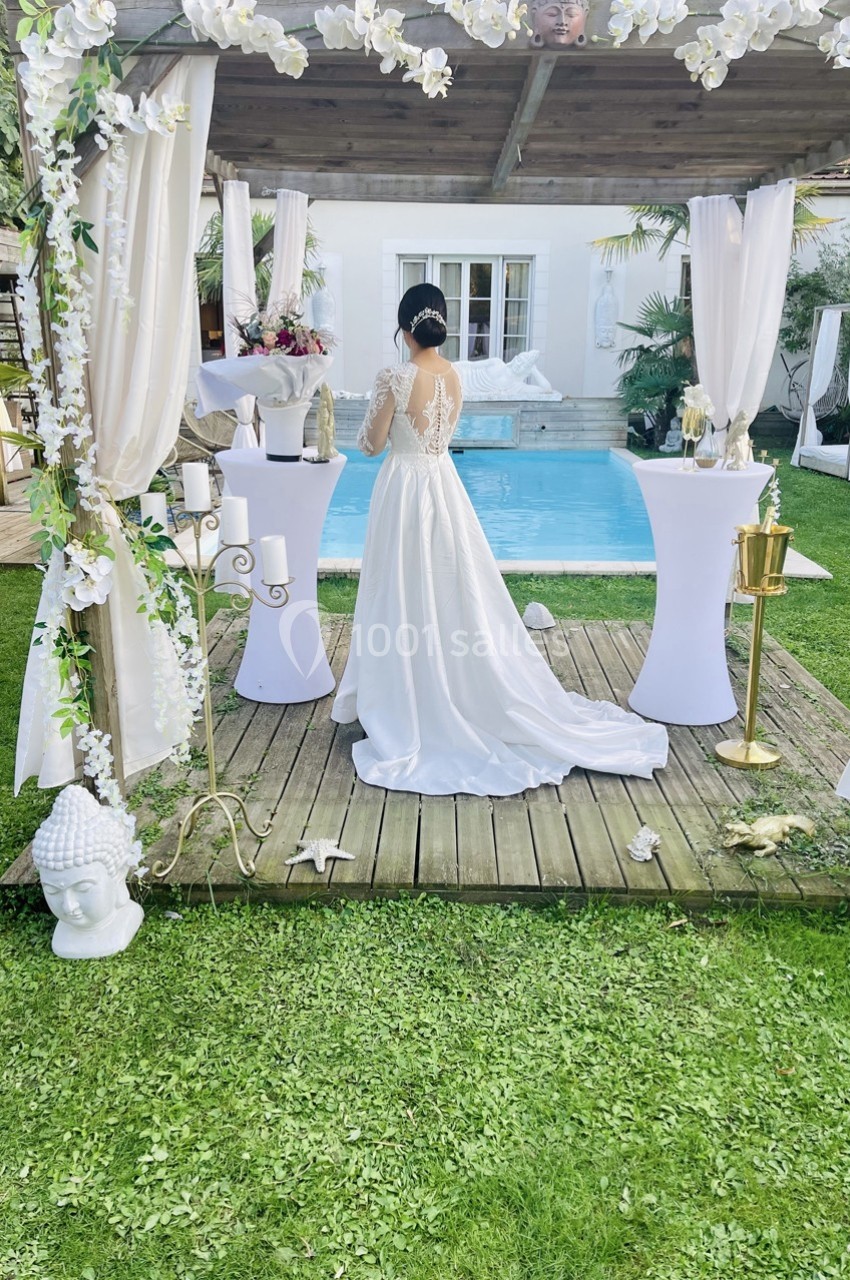 Une femme en robe de mariée blanche se tient dos à une piscine, entourée de décorations florales et élégantes.