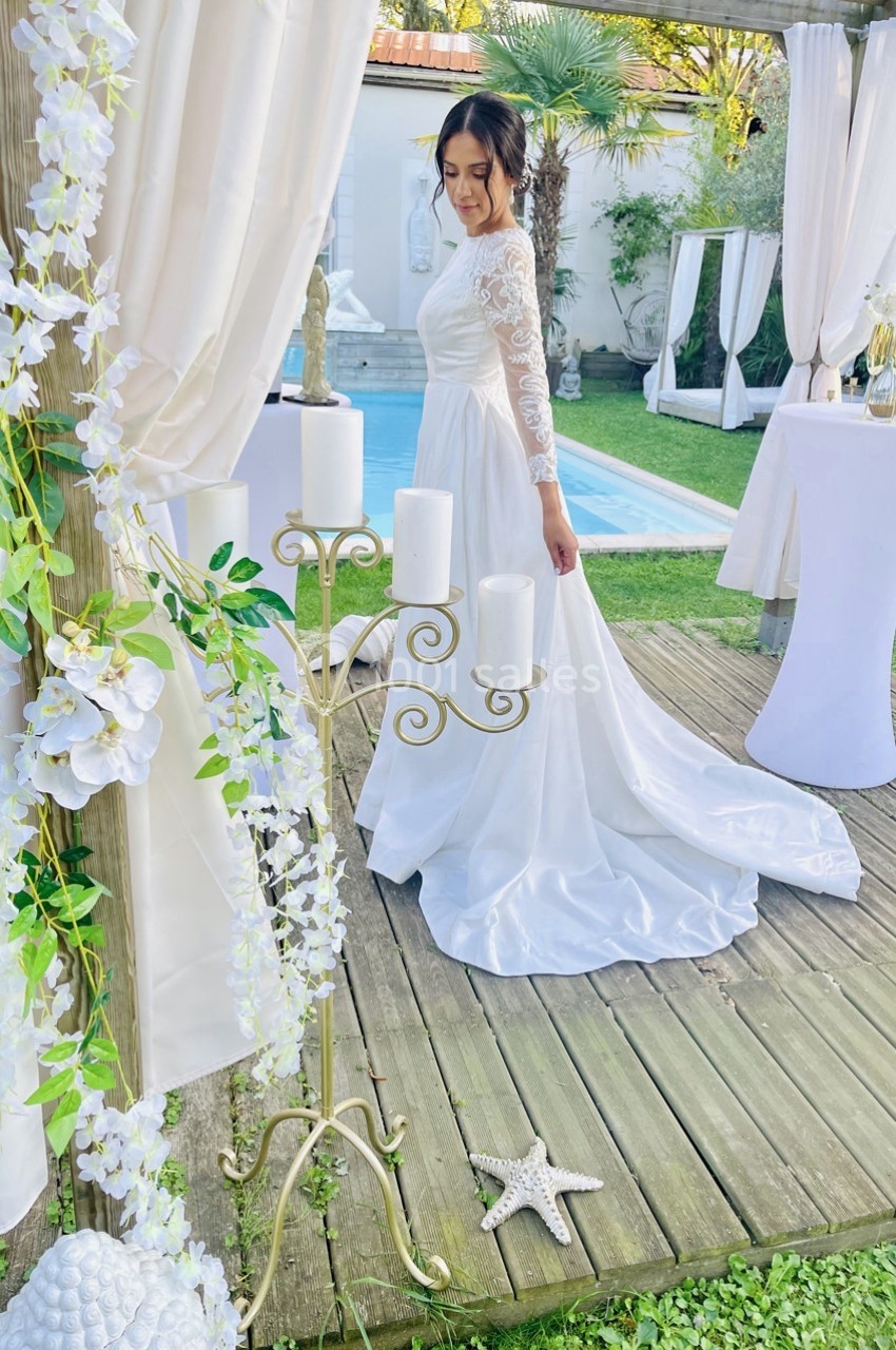 Une femme en robe de mariée blanche se tient sur une terrasse en bois, entourée de décorations florales et de bougies.