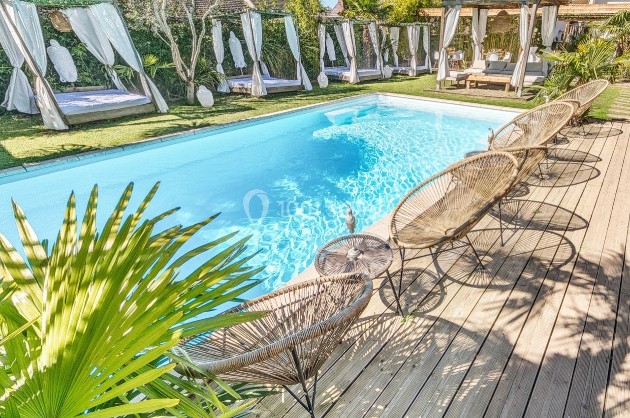 Piscine extérieure entourée de transats en rotin, lits balinais et végétation dans un cadre ensoleillé.