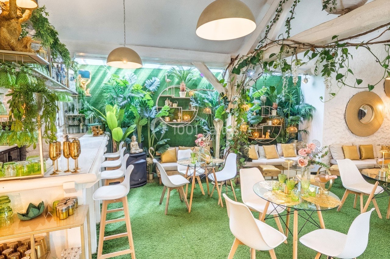 Espace lumineux et végétalisé avec mobilier moderne, tables en verre, chaises blanches et décor tropical.