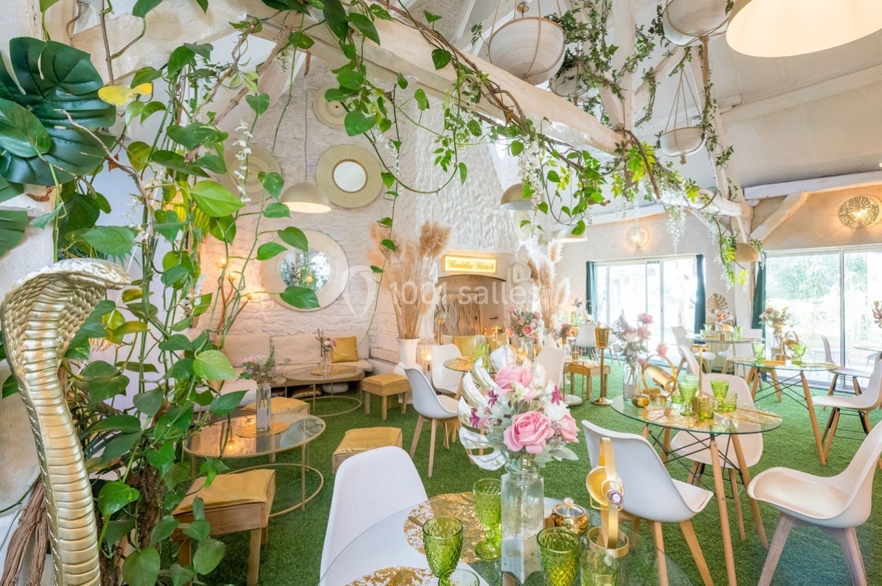 Salle lumineuse décorée de plantes, de fleurs et de mobilier moderne, avec des tables en verre et des chaises blanches.