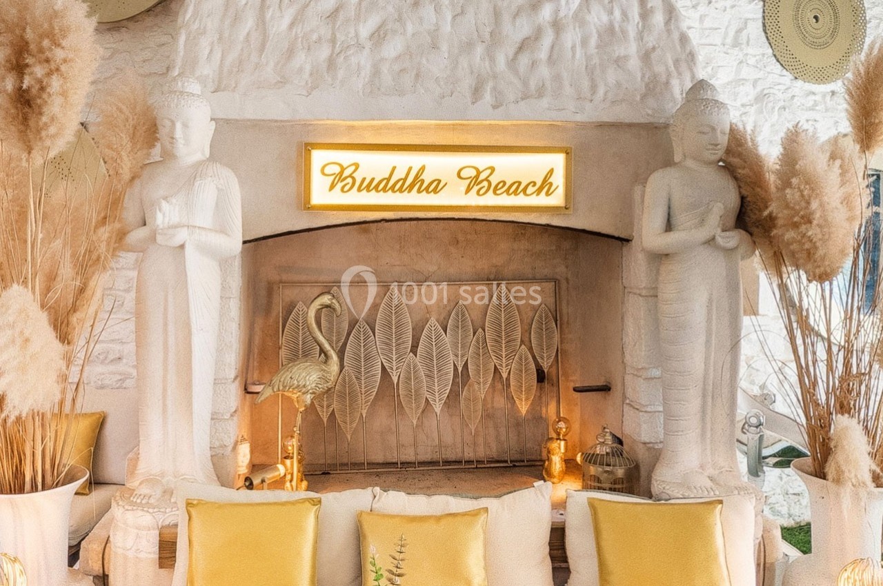 Deux statues de Bouddha encadrent une cheminée décorative avec un panneau lumineux ’Buddha Beach’.