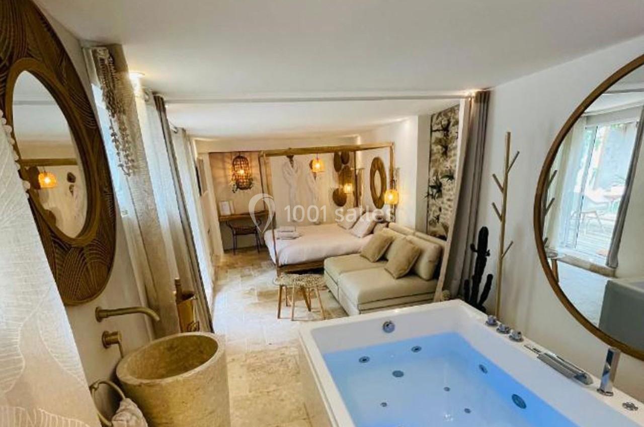 Chambre lumineuse avec lit double, canapé, jacuzzi intégré et décoration naturelle aux tons clairs.