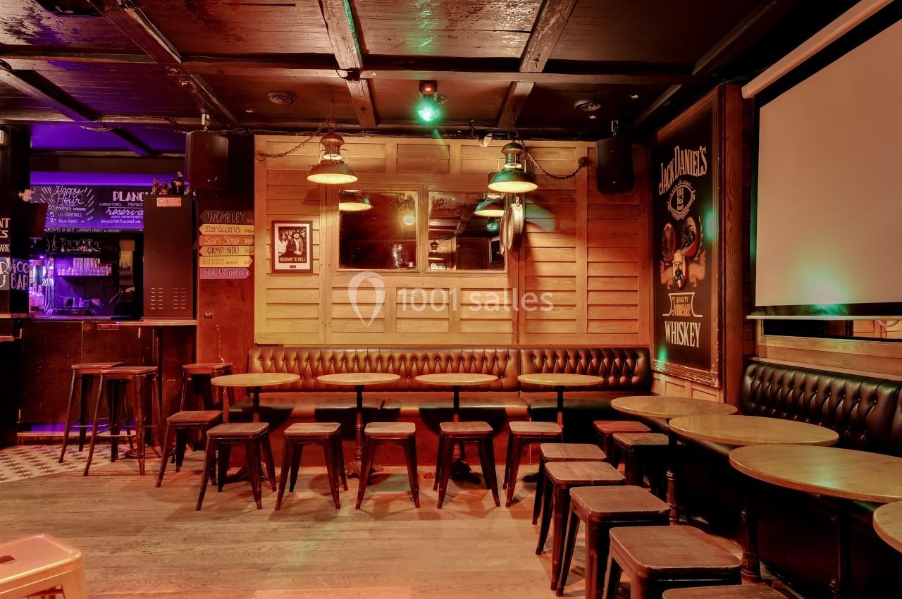 Salle de bar avec tables en bois, tabourets alignés et éclairage tamisé dans une ambiance chaleureuse.