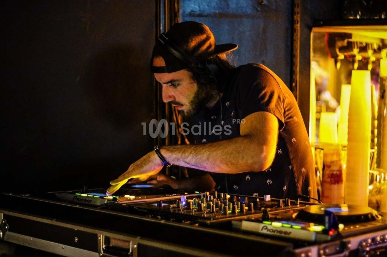 Un DJ mixe de la musique sur une table de mixage dans une ambiance sombre et lumineuse.