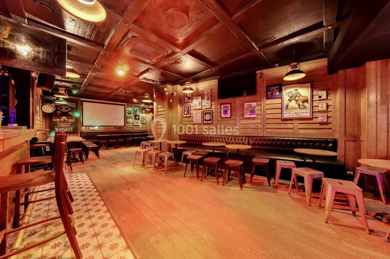 Intérieur d'un bar chaleureux avec des tables en bois, des tabourets et une décoration murale rétro.