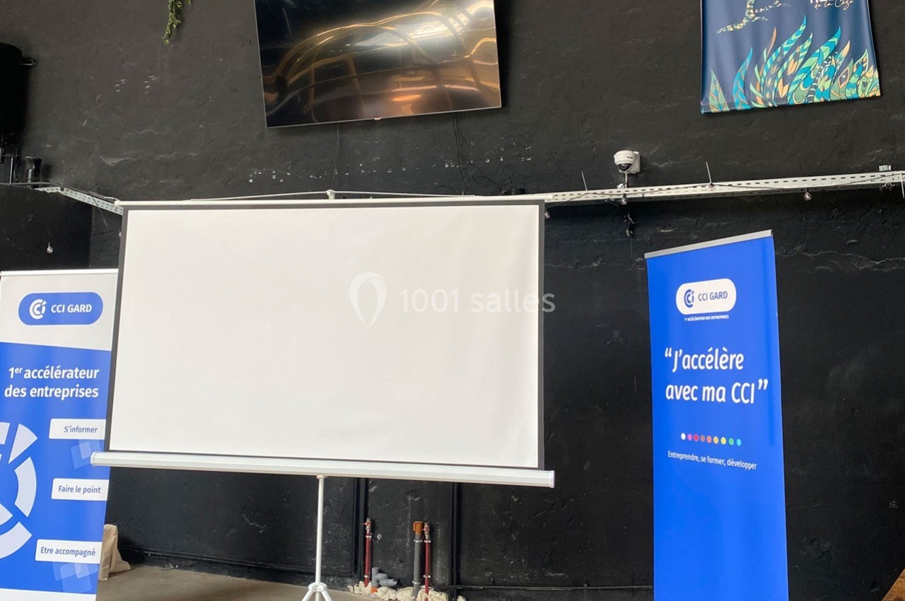 Écran de projection blanc installé dans une salle avec des affiches et des supports promotionnels de la CCI Gard.