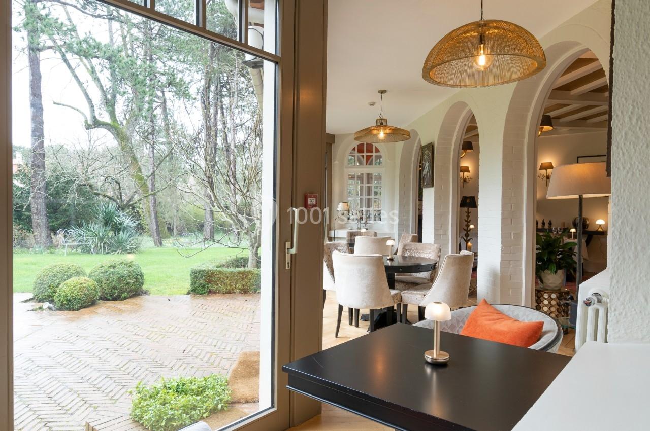 Salle à manger lumineuse avec grandes baies vitrées, vue sur un jardin, meubles élégants et décorations chaleureuses.