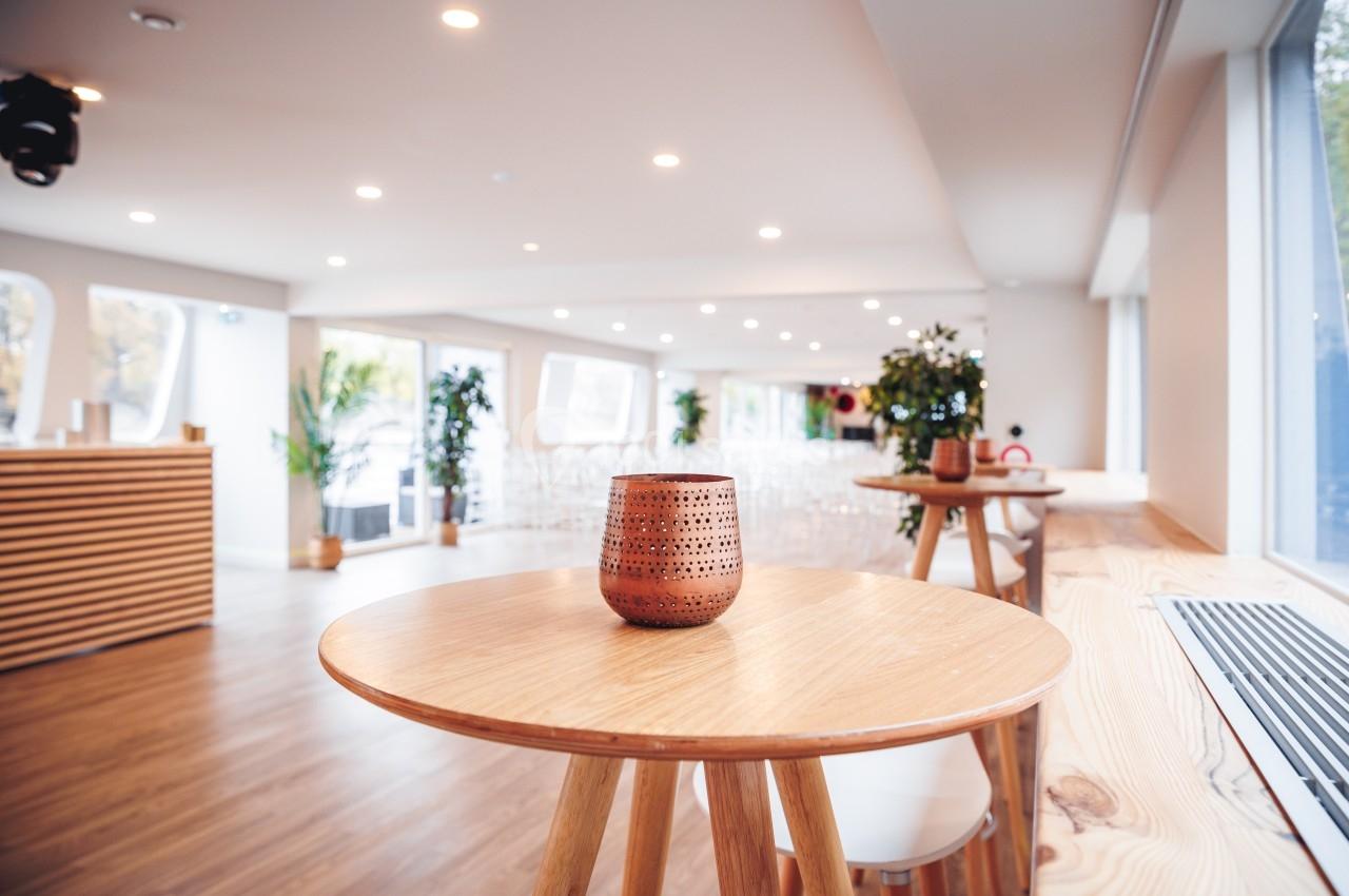 Salle lumineuse avec tables en bois, bougie décorative au premier plan et plantes en arrière-plan.