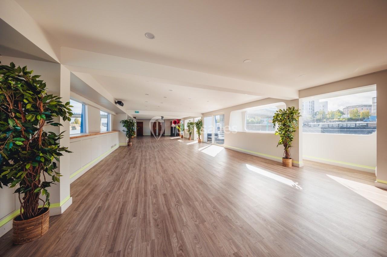 Salle lumineuse avec parquet, grandes fenêtres laissant entrer la lumière naturelle et plantes en pots.